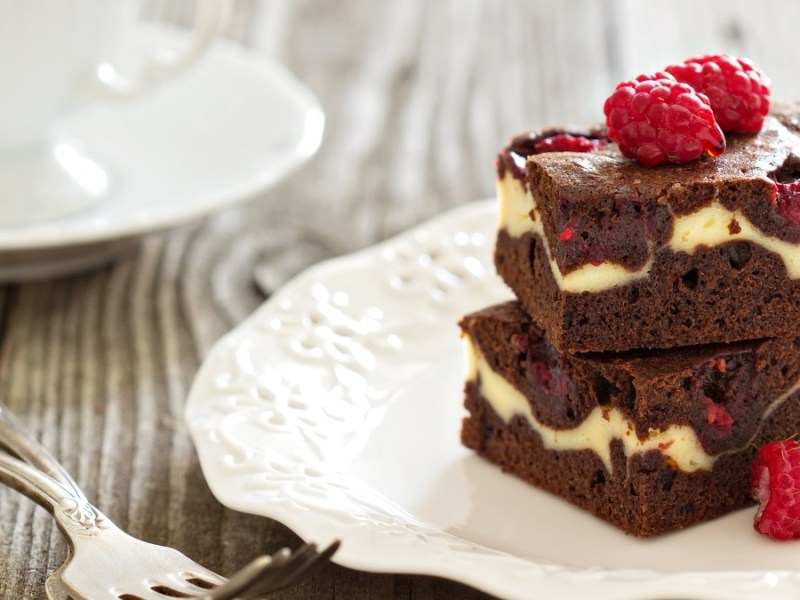 Dos brownies de cheesecake con frambuesas uno encima del otro en un plato.