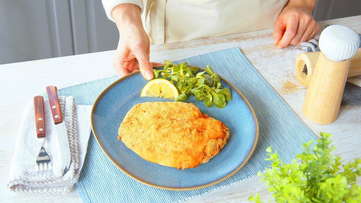 Un cordon bleu con salami en un plato azul. En el plato hay una rodaja de limón y un poco de canónigos. Junto al plato hay cubiertos y un salero y pimentero.