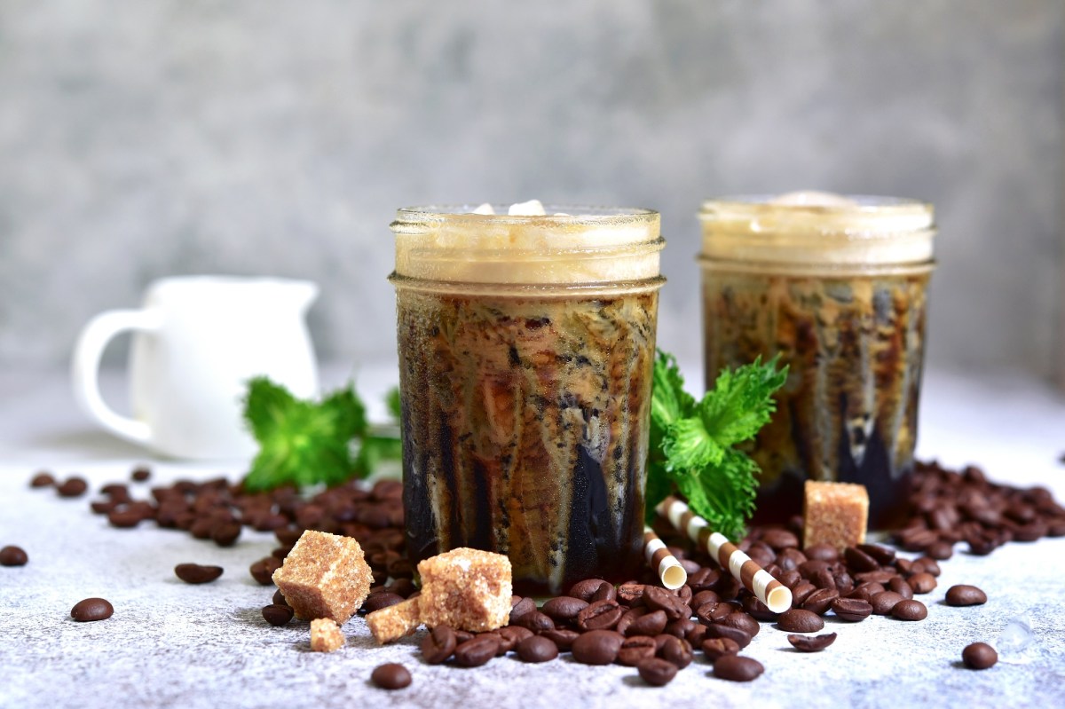2 vasos de frappé griego, rodeados de cubos de azúcar y granos de café.