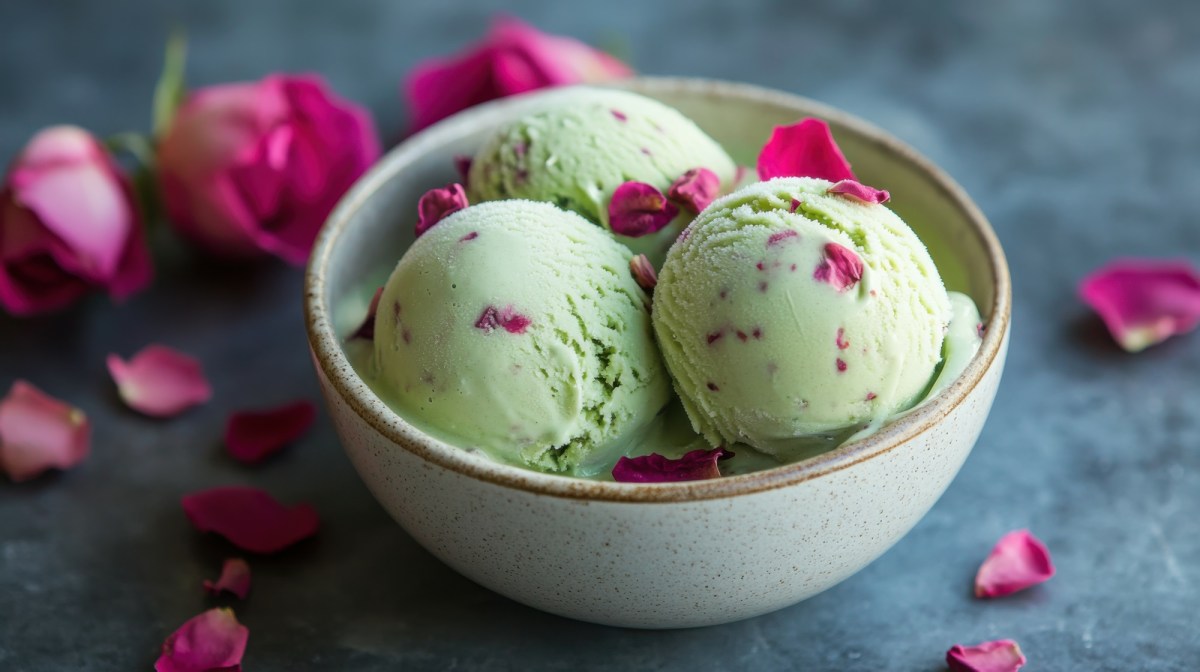 Tres bolas de helado de pistacho y rosas en un tazón verde claro.