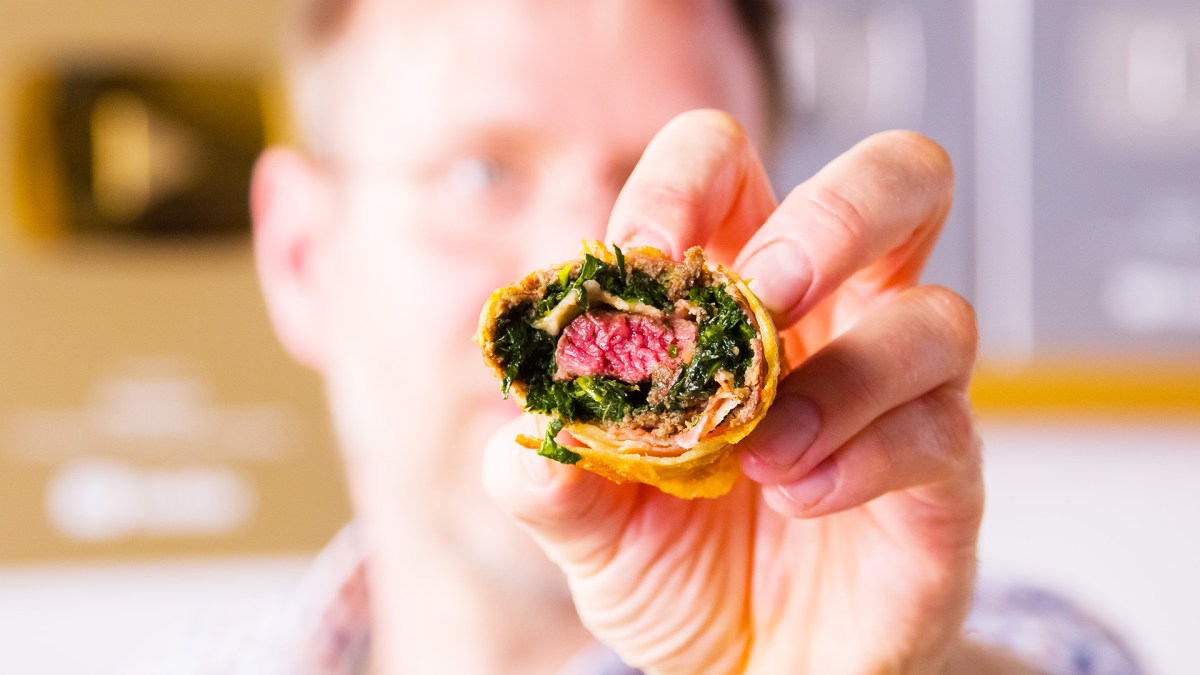 Se sostiene un rollito de primavera Beef Wellington hacia la cámara, mostrando el relleno.