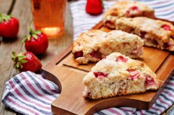 Scones de fresa y suero de leche en una tabla, fresas y un paño de cocina a rayas.