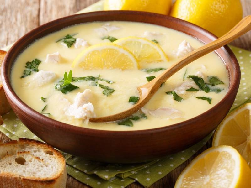 Un tazón con sopa de limón amarilla, una cuchara y rodajas de limón como decoración