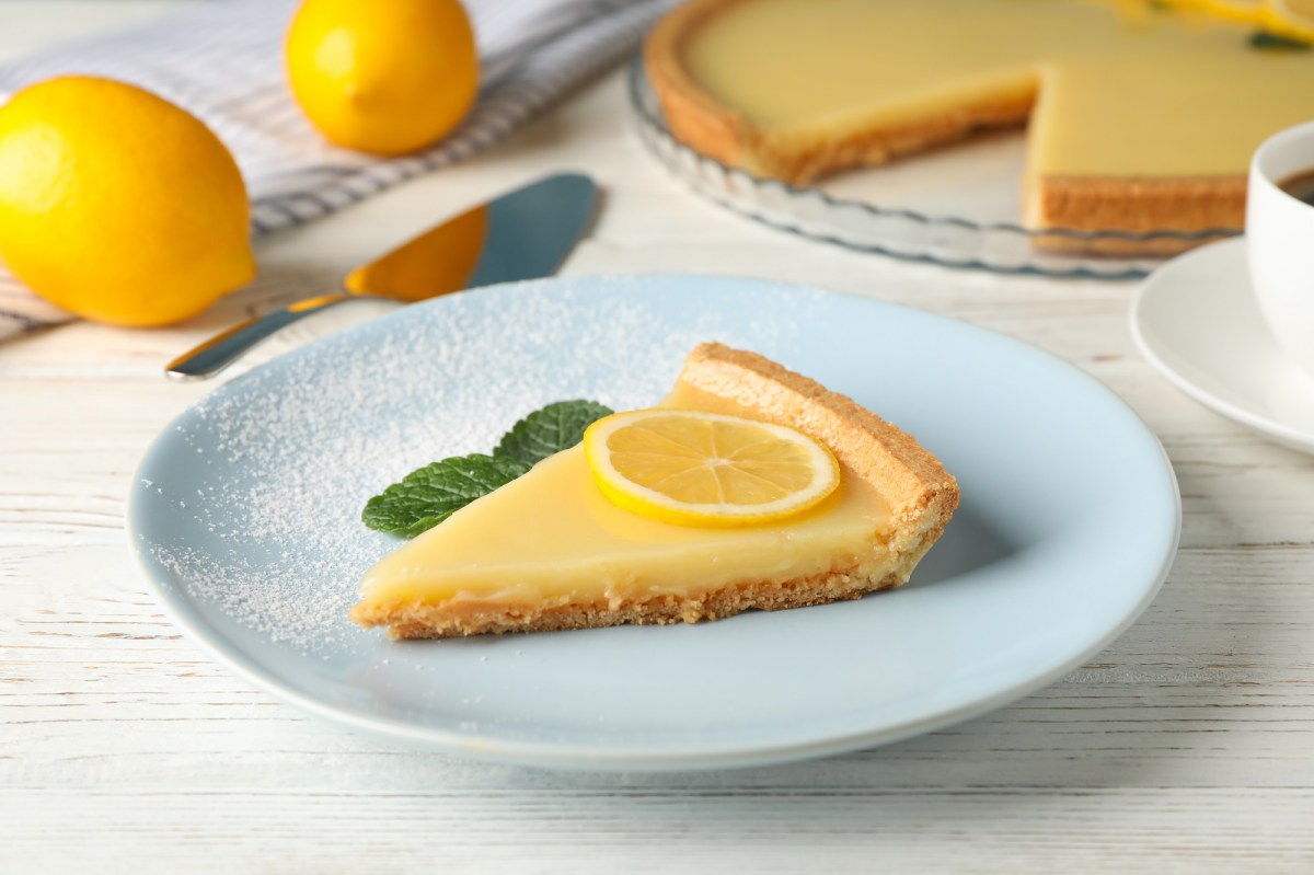 Tarta de limón, adornada con menta y una rodaja de limón, en un plato azul claro. Al fondo, borroso, el resto de la tarta.