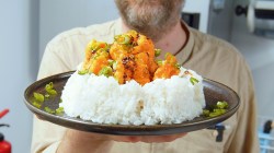 Un plato con una porción grande de arroz, sobre el cual se distribuyen los camarones Bang Bang. El chef Oli sostiene el plato hacia la cámara.