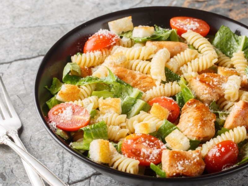 Un plato de ensalada César con pasta, junto al cual hay dos tenedores.