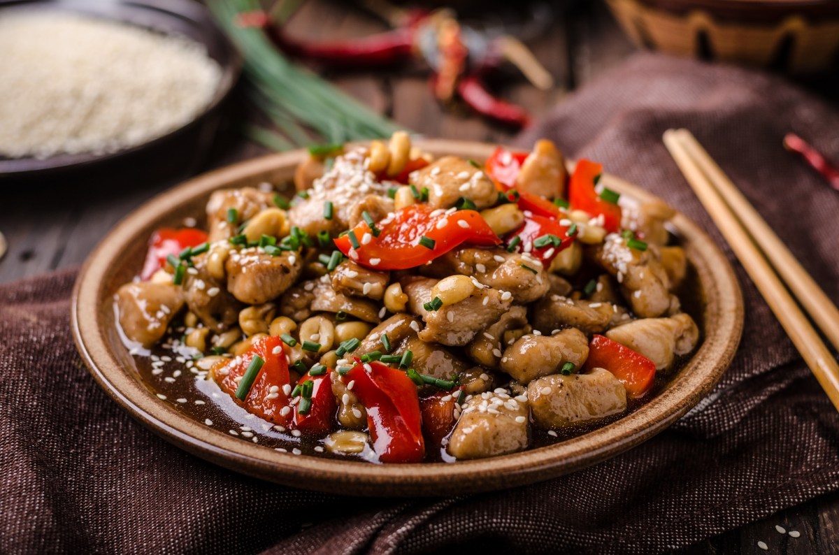 Pollo Kung Pao en un plato marrón claro. Junto a él hay palillos