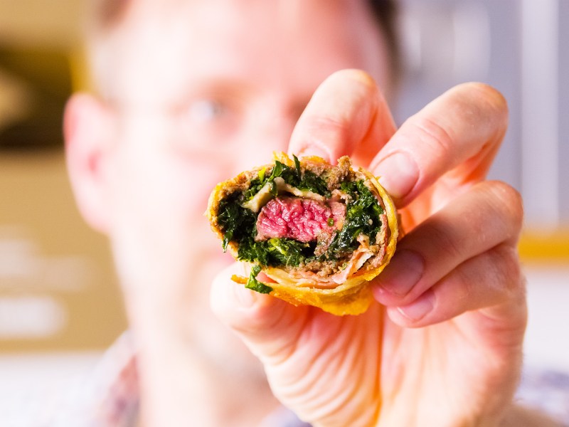 Se sostiene un rollito de primavera Beef Wellington hacia la cámara, mostrando el relleno.