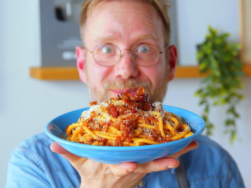 El cocinero Oli sostiene un plato de Bucatini all'Amatriciana hacia la cámara.