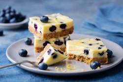 Varias porciones de pastel de queso con limón y arándanos sin azúcar en un plato. Alrededor hay arándanos.