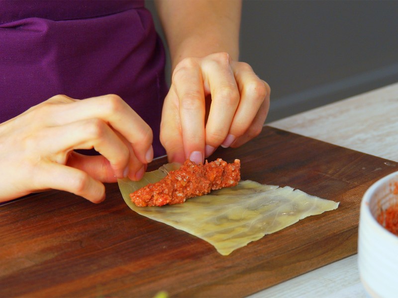 Cocinera enrolla el relleno de carne molida en una hoja de repollo blanqueada.