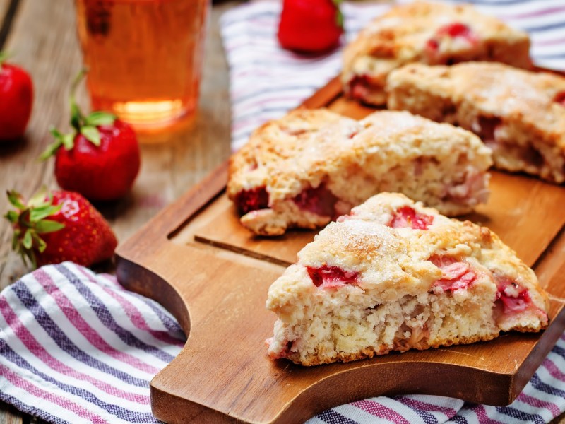Scones de fresa y suero de leche en una tabla, fresas y un paño de cocina a rayas.