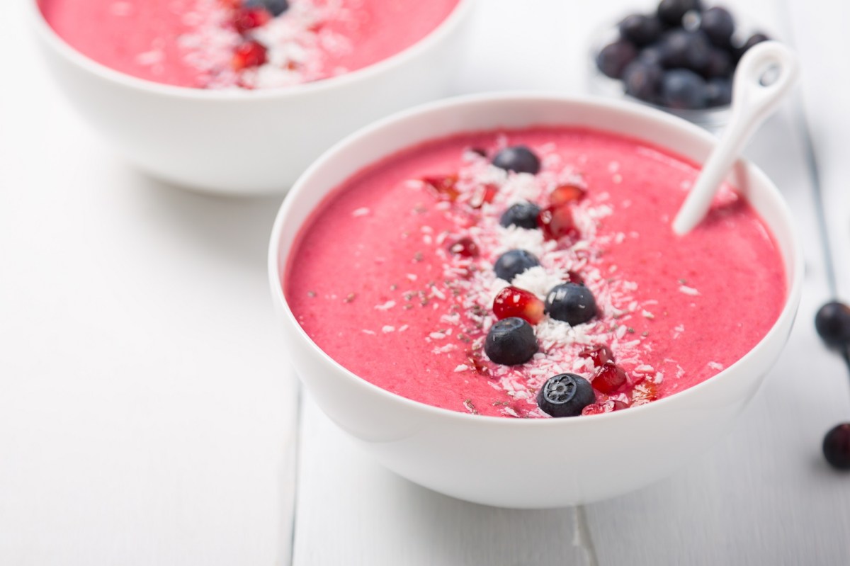 2 tazones de smoothie de fresa decorados con arándanos azules, coco rallado y semillas de granada.