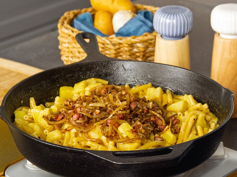 Älplermagronen con cebollas fritas en una sartén de hierro fundido.