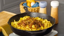 Älplermagronen con cebollas fritas en una sartén de hierro fundido.