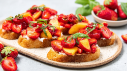 Bruschetta de fresa y nectarina, presentada en una tabla. En primer plano hay una fresa, al fondo se ve un cuenco con las bayas.