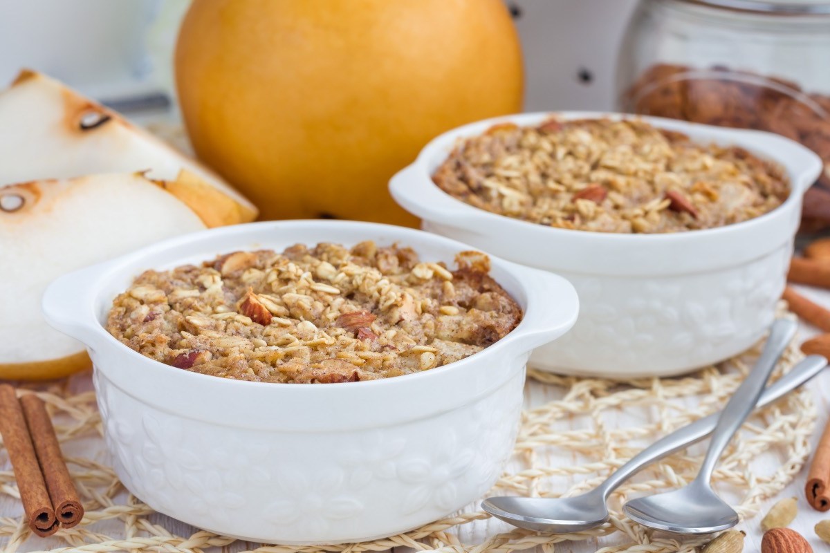 Dos pequeños moldes con gachas de avena al horno. Al fondo hay peras frescas.