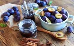 Varios frascos de mermelada de ciruelas al horno. Alrededor hay ciruelas frescas y utensilios.