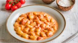 Un plato de ñoquis en salsa de tomate y coco sobre una mesa, con tomates frescos a un lado