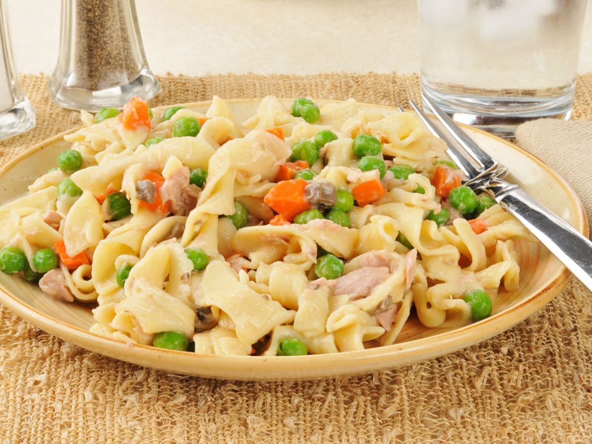 Pasta con atún y guisantes y zanahorias en un plato. Junto a él hay cubiertos.