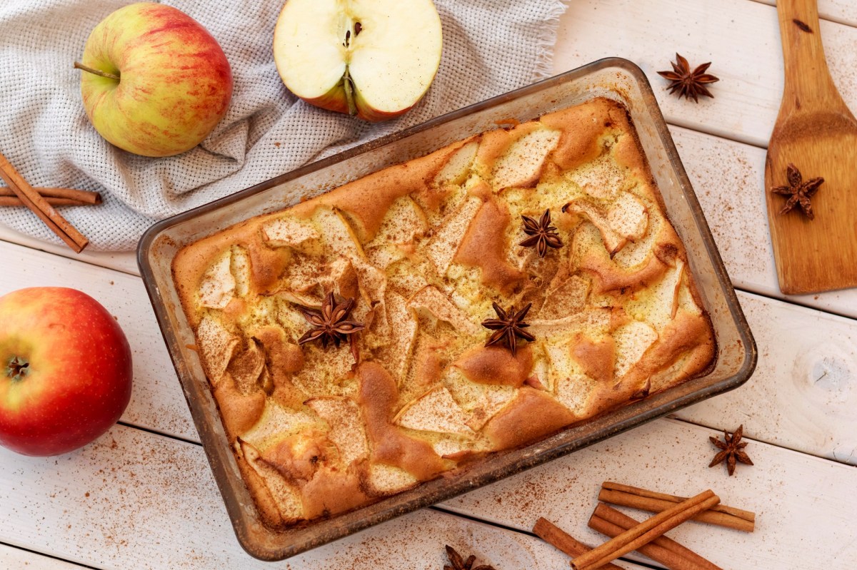 Pastel de manzana en una fuente para hornear rectangular, vista superior. Alrededor hay manzanas, ramas de canela y estrellas de anís.