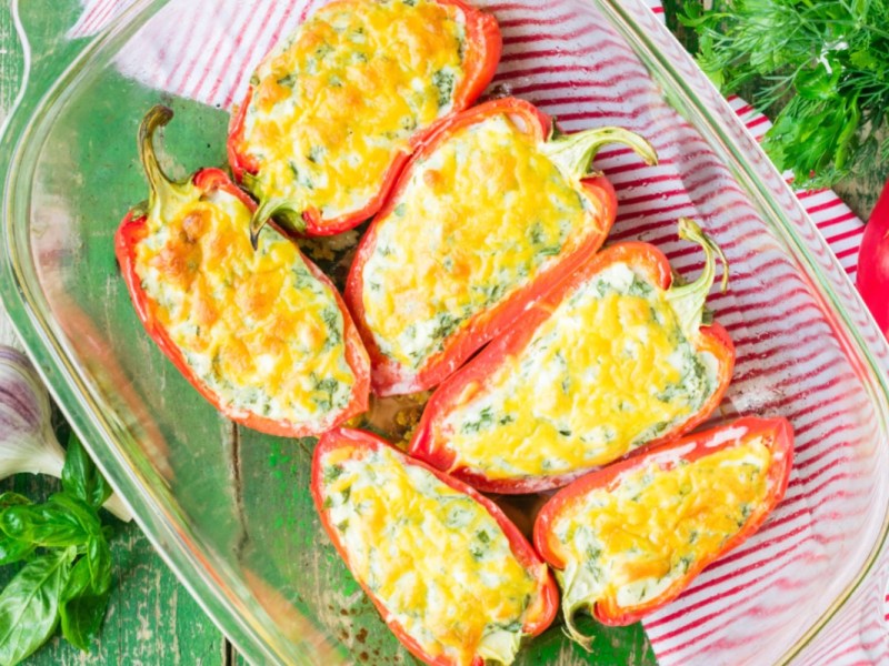 Pimientos rellenos de queso feta y arroz en una fuente transparente para horno vistos desde arriba.