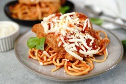 Pollo a la parmesana, servido con espaguetis, en un plato gris.